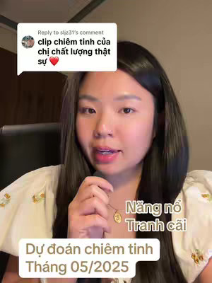 A medium shot features a young woman with long, dark hair and fair skin centered in the frame. She wears a white blouse with floral embroidery and a delicate gold necklace with a round pendant. The background is a blurred interior setting. Overlay text indicates the video content is related to astrology, specifically predictions for May 2025.