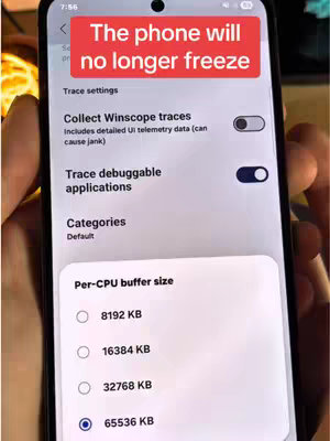 The image shows a smartphone screen displaying settings related to performance, specifically 'Trace settings' with options for 'Collect Winscope traces' and 'Trace debuggable applications.' A red bar at the top features white text stating 'The phone will no longer freeze.' The screen is held by a hand, with the focus on selecting a 'Per-CPU buffer size'.