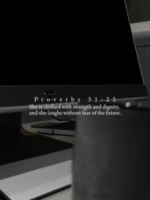 The image displays a dark workspace with a computer monitor as the central focus. The monitor is turned on, displaying a black screen. Overlayed on the image are white text elements presenting a Bible verse, which adds a spiritual element to the composition. The background appears to be a desk setup in a dimly lit room, with other objects visible to the left. The overall tone is somber and simple with vertical orientation.