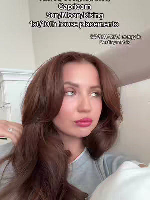 A young woman with long, wavy brown hair is the central focus of the image. She has a fair complexion, pink lipstick, and is looking off to the side with a slight gaze. Text overlays display astrological information at the top and bottom right.