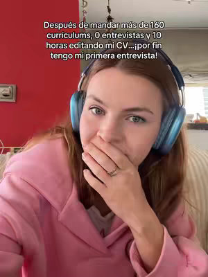 A woman in a light pink jacket is shown in a close-up, covering her mouth in a gesture of surprise or anticipation. She wears large blue headphones. Text appears above in Spanish, describing her job search efforts.