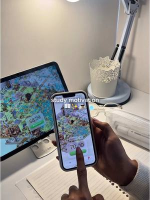 A person is holding a phone, the screen displays a timer; a tablet shows a map, the room is bright, with a desk lamp, a pen holder, and a book .