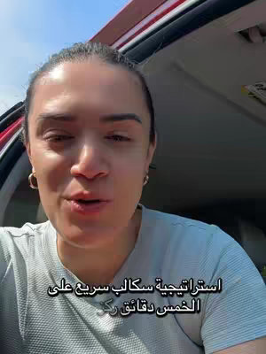 A woman is filmed from the chest up. The background shows the interior of a vehicle and partly the sky. She has dark hair and is wearing gold hoop earrings. The text overlay is in Arabic.