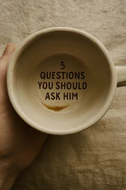 The cover image shows the inside of a white ceramic mug. Inside the mug, centered, is the text "5 QUESTIONS YOU SHOULD ASK HIM" in dark brown letters. There's some brown residue at the bottom of the mug. A hand is holding the mug to the left side of the frame, against a tan and brown patterned surface.