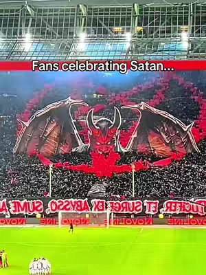 A stadium is filled with people and a large banner depicting a red devil figure with flames in the background. Text overlay reveals the phrase, 'Fans celebrating Satan...'