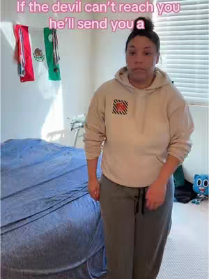 A woman stands in her room, facing the camera. The upper portion of the image shows text. Decorations hang on the upper left wall. The background includes a bed on the left, a window with blinds on the right, and various items in blurred focus.