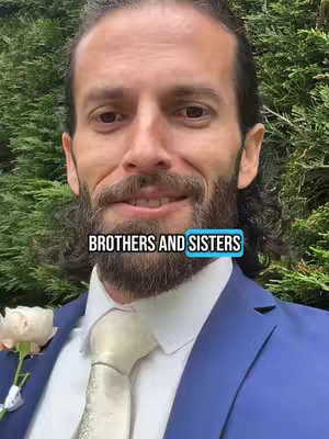 A medium shot of a man in a blue suit smiling at the camera, with his head and shoulders visible. The background has a lush green foliage. Text overlayed on the image reads: BROTHERS AND SISTERS.