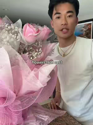 A young man in a white t-shirt is holding a large bouquet of pink flowers, with text overlayed.