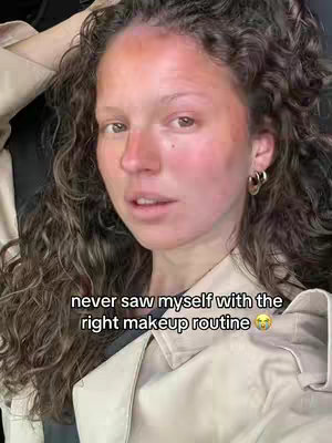 A woman with curly brown hair is looking towards the camera. She has makeup on, with flushed cheeks and a hint of shadow around her eyes. The top of her hair is lightly touching her head.