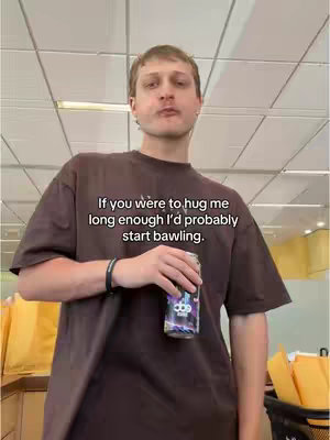 A man stands in front of a grid of ceiling lights and yellow envelopes. The man is wearing a reddish-brown t-shirt, and he is holding a can. Text overlay has been added to the image.