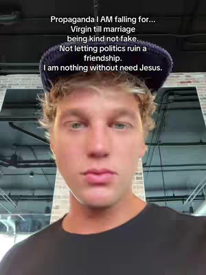 A young man with fair skin and short, light brown hair is centered in the frame. He wears a black shirt and a dark blue cap. The background suggests an indoor setting potentially a studio or office space. Text overlays the image in a readable font stating various beliefs the person has.