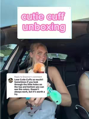 A young woman is seated inside a car holding several colorful plush toys. Above her head, a white rectangle with the words "cutie cuff unboxing" in pink letters hovers. The woman smiles, looking towards the camera.