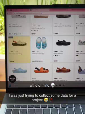 A laptop screen displaying a webpage featuring various Crocs shoes. The screen is angled slightly upward, with a keyboard visible below. Overlay text adds emphasis, and a background of a window is visible.
