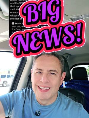 A man in a blue shirt smiles at the camera while seated in a car. Above his head is a large pink and purple graphic that says "BIG NEWS!". In the top-left corner, partial text is visible. The background shows a white car and the interior of the vehicle.