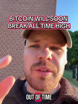 A man with a short beard and a hat is centered in the frame. Text overlays read 'BITCOIN WILL SOON BREAK ALL TIME HIGH' at the top and 'OUT OF TIME' at the bottom. Behind him is a brick wall on the left, with a glimpse of greenery and a road on the right under a clear sky.