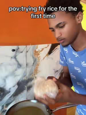 A young man in a blue shirt is facing toward the camera, with a stove and frying pan in the background. Text overlay reads 'pov: trying fry rice for the first time'.