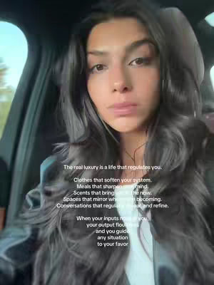 A woman with long dark hair is seen from the chest up, slightly angled. She is in a car with a black interior, and the image is well-lit. Superimposed on her is white text in a sans-serif font, discussing luxury as a life of regulation.