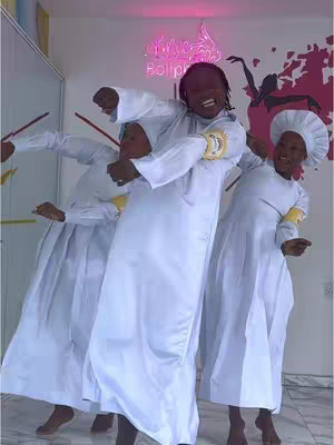 Three people dressed in white, seemingly religious clothing are captured in a dynamic pose, looking towards the camera with expressions of joy. They are in a brightly lit space, possibly a studio or performance area, with vibrant pink neon signs above them, while a colorful graffiti art piece adorns the wall behind them. The composition suggests a celebratory moment, with all of them wearing head coverings and wristbands. One person is in the middle, with another person on each side in various poses and gestures. 