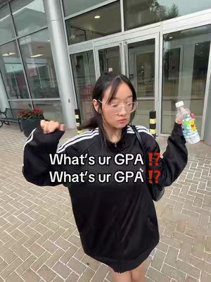A young woman stands outside a building, dressed in a black Adidas jacket, and holding a water bottle. The background includes glass doors, brickwork, and greenery. Overlaid on the image is bold white text with red exclamation marks, asking 'What's ur GPA?'