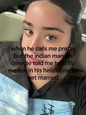 A selfie-style shot, the creator is centered with the camera at a close range. The focus is on the face and upper chest, with the background slightly blurred. The face takes up most of the frame. The skin tone is fair, and the hair is black, pulled back. The expression appears thoughtful. Written text is overlaid on the image against the creator's face.