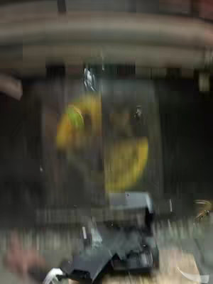 The cover image is a blurry, abstract shot. The background appears to be dark, possibly black or a very dark color, with a suggestion of an interior setting. Towards the bottom, there is a black object and another light colored object, likely either a part of the car or an object on the ground. The yellow or orangish shape is a blurry form which can be related to a wheel-like setting.