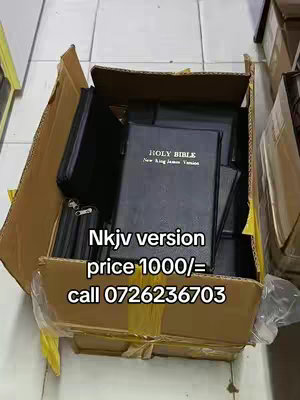 A box filled with several black Bibles is prominently displayed. The Bibles are stacked and slightly angled, with some open to reveal the text. The box itself is cardboard, marked with tape and a label indicating "Nkjv version price 1000/= call 0726236703". The text overlay provides purchasing information, and the overall composition is functional.