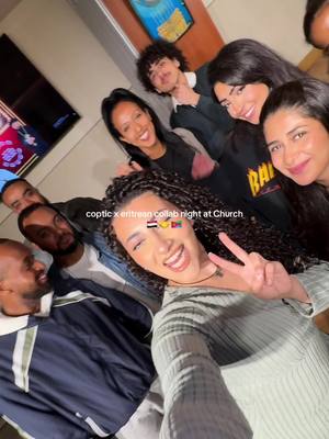 A selfie-style photo featuring a group of diverse individuals. The primary focus is on a smiling woman in the foreground holding up a peace sign. The background includes other people also smiling, and the setting appears to be indoors, potentially at a church gathering given the caption. Text overlays are added for context.