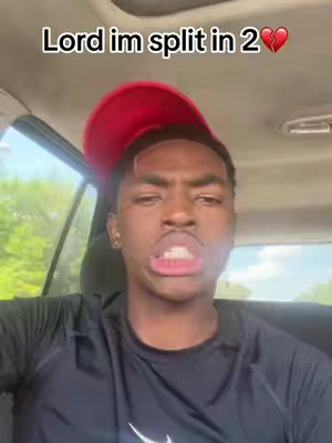 A young Black man wearing a red baseball cap and a black shirt is inside a vehicle's front seat. Text overlaid at the top says, "Lord im split in 2". The man has a slightly shocked or surprised expression, with slightly parted lips.