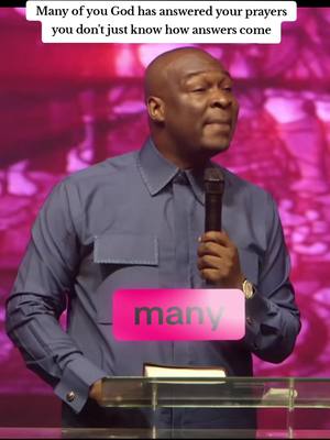 A man in a blue shirt speaking at a podium with a microphone. The background is blurred with pink and purple tones. Overlay text says 'Many', inside a pink rectangle.