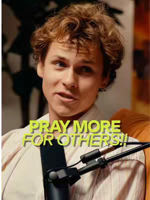 A young man with curly brown hair and a light complexion is centered in the image, looking towards the left with a slight smile. He is wearing a collared shirt and what appears to be a robe or jacket. The background is blurred but appears to contain warm tones. Overlaid on the image is the text \"PRAY MORE FOR OTHERS!!\" in a yellow-green font.