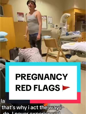The image shows a man in a hospital room, wearing a tank top and bucket hat, looking towards a person seated on the floor, partially out of view. Text reading 'PREGNANCY RED FLAGS' with a red flag icon is overlaid at the bottom. The setting suggests a hospital room with medical equipment present.
