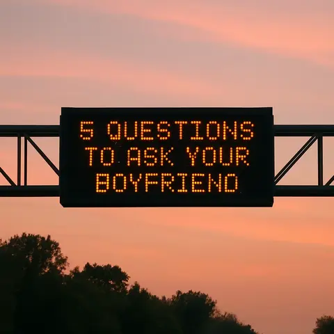 The image shows a highway sign displaying the message "5 QUESTIONS TO ASK YOUR BOYFRIEND" in glowing orange letters against a pink and orange gradient sky. The sign is mounted on a metal structure, with hints of trees visible at the bottom. The warm-toned sky suggests either dusk or dawn.