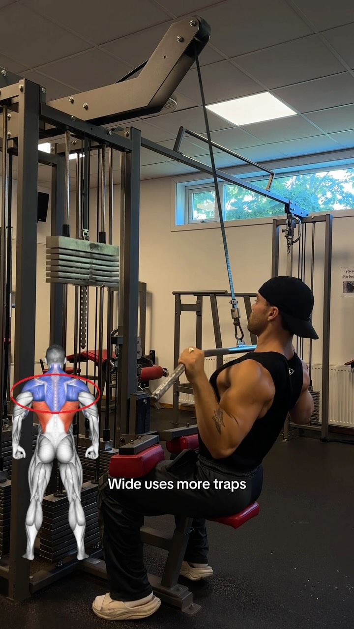 The image shows a man working out at a gym using a lat pulldown machine.  A diagram overlay highlights back muscles. Text overlay reads 'Wide uses more traps'. 