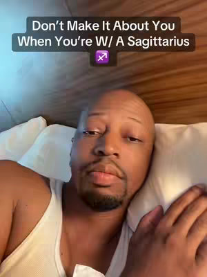 A man with a bald head and a short beard is lying in bed, looking directly at the camera. Text overlayed on the top suggests the video is about astrological signs. The background has a warm, interior hotel feel.