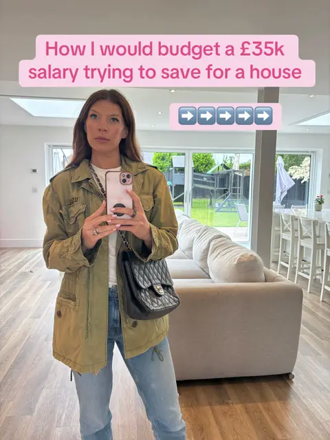 A woman stands in front of a modern living room, holding a phone. Text overlays at the top read 'How I would budget a £35k salary trying to save for a house' and a series of right-facing arrows are below. The woman is wearing a green jacket, jeans and a white tee. She is wearing a black chain bag, and the scene includes a modern sofa and view of a garden.