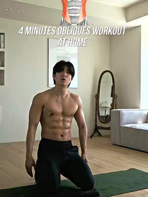 The image displays a man with a muscular physique kneeling on a green mat. Text overlaid at the top indicates the video content. The setting appears to be a well-lit room with mirrors and a couch in the background.