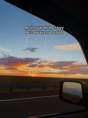 An image taken from inside a car, looking out at a scenic sunset. The sky is filled with orange and pink hues, while the foreground shows a road and the side mirror of the car. Text overlay on the image.
