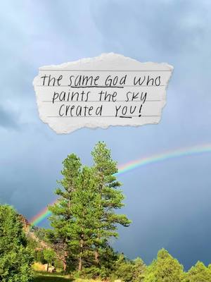 The image shows a landscape with a rainbow, some trees, and a piece of paper with text. The sky ranges from dark blue to light blue. A rainbow arcs across the sky. In the foreground are green trees and foliage. A piece of torn paper against the sky contains handwritten text.