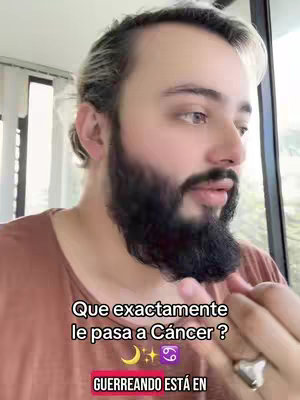 A man with blonde-streaked hair and a dark beard is looking off-camera. Text overlays read, 'Que exactamente le pasa a Cáncer?' (What exactly happens to Cancer?) which is followed by a crescent moon, a sparkle, and the Cancer astrology symbol.