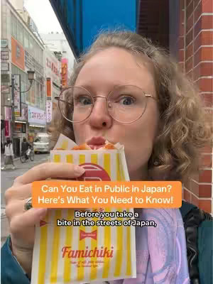 A woman with curly blonde hair and glasses is holding up a wrapped and printed paper with the words "Famichiki" visible. The background is a crowded street with buildings and signs.