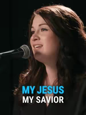 A woman with brown hair is singing into a microphone. The background is dark. Text overlay at the bottom reads "MY JESUS, MY SAVIOR."