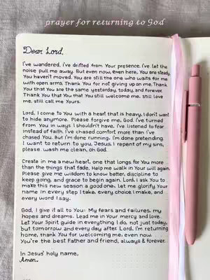 An open notebook displays a handwritten prayer on a white page, with a pink pen and ribbon bookmark placed to the right. The text is the focus. The notebook is set against a soft, neutral-toned background.