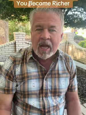 A man with gray hair and a beard is speaking directly to the camera. He is wearing a plaid shirt, and there is text overlaid at the top of the image. The background includes a brick structure and foliage.