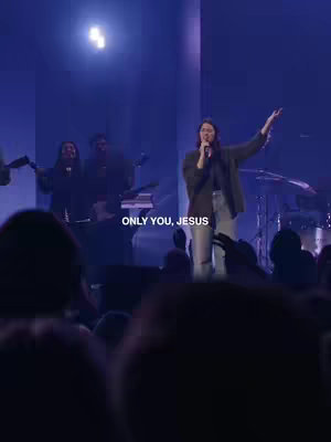 A woman is singing on stage with her arms raised, a microphone in hand. The background is a concert setting with stage lighting and other musicians visible behind her. The text "ONLY YOU, JESUS" is overlaid on the image.