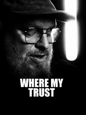 A black and white image featuring a man with a beard, glasses, and a hat. The image is a close-up, with text overlayed at the bottom.