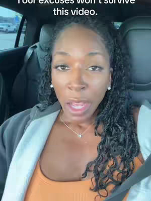 A selfie-style video in a car shows a Black woman with long, braided hair in a casual setting. She is wearing an orange top and a black jacket. Her facial expression is serious, with her mouth open as if she's speaking and the background blurry.