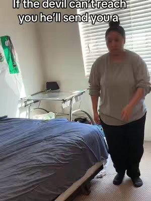 A woman stands in a room with a bed, a table, and a window with blinds; a text overlay appears at the top of the image.