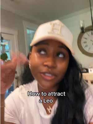 A woman with dark hair and a white and tan baseball cap is looking upwards as she speaks. Text overlay reads 'How to attract a Leo'.