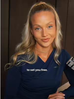 A woman with long blonde hair and blue eyes gazes at the camera. She is wearing a dark blue v-neck shirt and a golden headband. In the bottom center, the text overlay is displayed. The background is a blurred brown.
