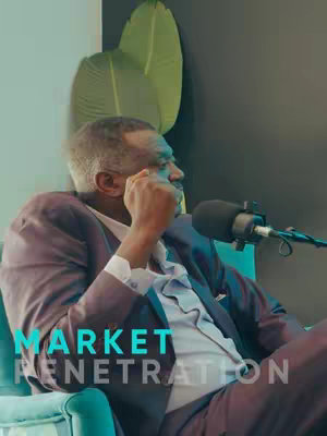 A man in a suit sits in an armchair with a microphone in front of him, as if in an interview setting. The background consists of a dark wall with large, stylized green leaves behind the man. Overlaid at the bottom left is the text "MARKET PENETRATION" in a turquoise font.